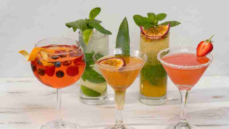 A vibrant selection of colorful cocktails arranged on a white table, featuring fresh fruits and garnishes., tags: feiertage - pexel